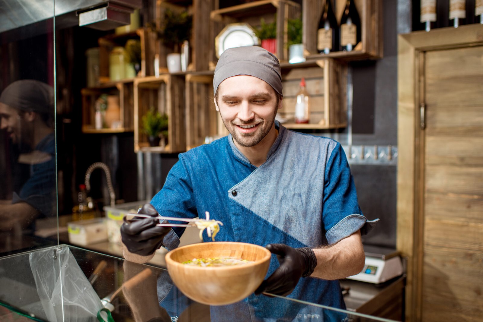 Portrait of caucasian chief cook in uniform decorating meal in the wooden plate at the asian restaurant kitchen